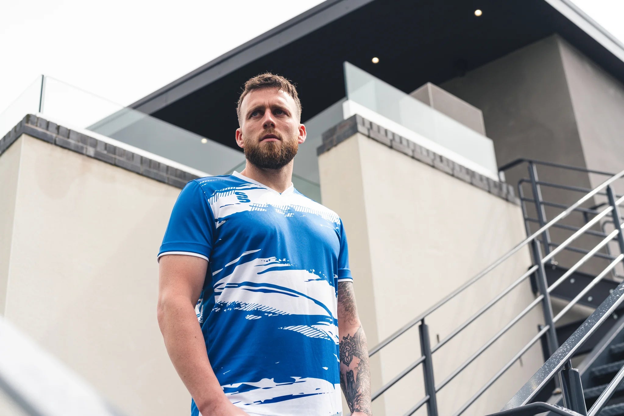 Man wearing a blue and white patterned shirt standing outdoors near modern architecture.